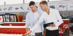 Two men stand beside a red tractor, smiling and engaged in conversation outdoors.