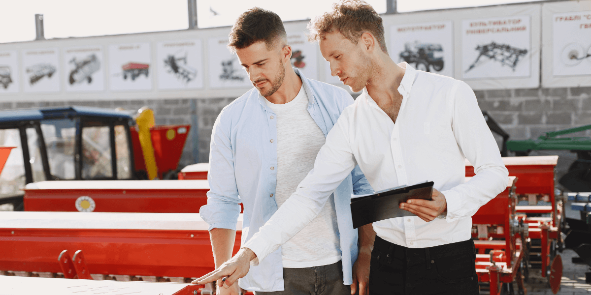 Two men stand beside a red tractor, smiling and engaged in conversation outdoors.