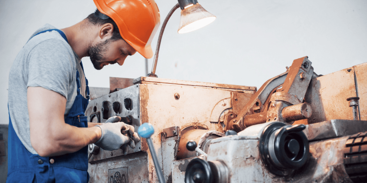 A man wearing an orange hard hat operates a machine, focused on his task in a work environment.