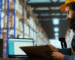 A man wearing a hard hat sits at a table, focused on his laptop, indicating a work-related environment.